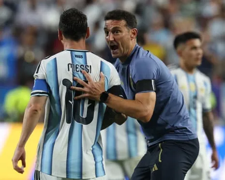 Coach Lionel Scaloni places his hand on Lionel Messi's back while speaking to him during a match.